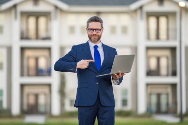 İş adamı dışarıda dizüstü bilgisayar kullanıyor. Erkek işadamı dizüstü bilgisayarı evin önünde tutuyor. Dizüstü bilgisayar kullanan bir adam. Beyaz tenli gözlüklü bir erkek bilgisayar ve açık hava portresi kullanıyor.