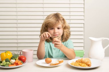 Çocuk yumurta yiyor. Yemek sırasında mutfakta sebze ve meyve yiyen bir çocuk var. Sağlıklı yemek, sebze yemeği.