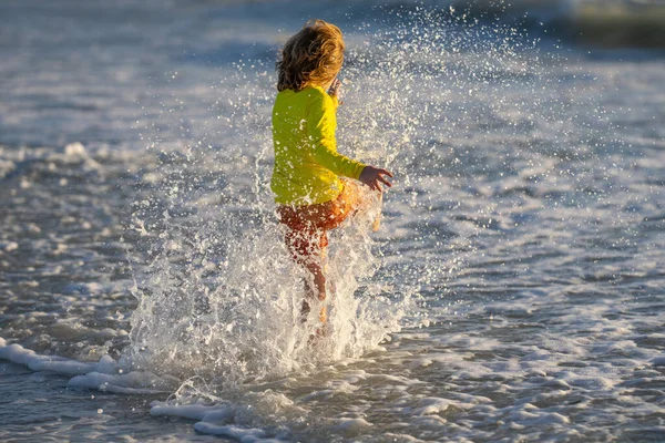 海に子供が飛び散った 子供は海の水のドロップで遊ぶ 小さな子供は水で遊んでスプラッシュを作る 子供は滴を楽しんでいます 夏休みに海の水の中に走っている子供 海に沿って走る子供の男の子 — ストック写真