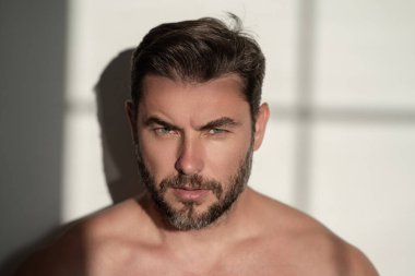 Çekici bir adamın erkek yüzü kozmetik reklamındaki krem için yakın plan portresi. Çıplak omuzlar, cilt bakımı, sağlık, cilt için kozmetik. Erkek güzeli. Traş, saç şekillendirme.