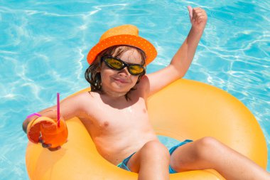 Kid floating in pool. Child relaxing in pool, drink summer cocktail. Summer holidays and vacation with kids. Happy little boy playing in swimming pool outdoor on hot summer day