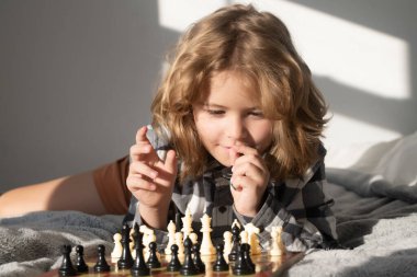 Little kid play chess. Thinking child. Chess game with children at home