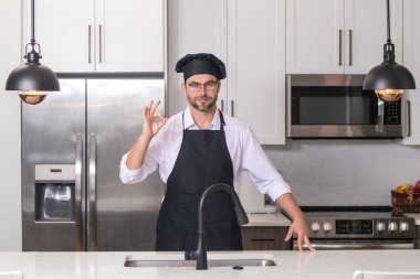 Chef cook with ok sign, delicious food. Portrait of chef man in a chef cap in the kitchen. Man wearing apron and chefs uniform and chefs hat. Character kitchener, chef for advertising