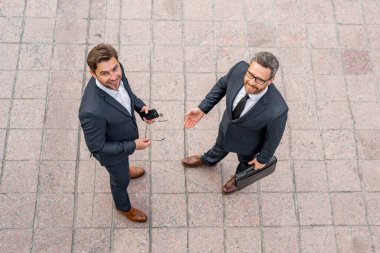 Top view of business man in suit talking about finance news standing in modern city. Businessmen walking and talking outdoor in New York city. Confident employee talk with colleague