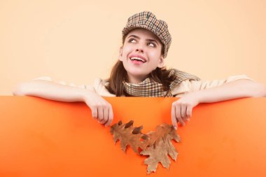 Güz sonbaharı modasına uygun giyinmiş hippi bir genç kadın şık bir şapka ve eşarp takıyor. Güzel kız sonbahar yapraklarını yüzüne yakın tutar, stüdyo arka planında izole olur. Akçaağaç yaprağıyla sonbahar kadınının portresi