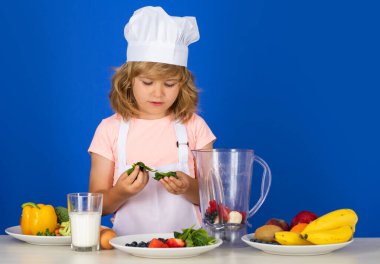 Şef şapkalı ve önlüklü çocuk yemek hazırlıyor. Mutfakta sebzeli küçük bir aşçı. Doğal çocuk yemekleri.