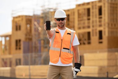 İşçi telefonu, inşaatçı telefon ekranı. Cep telefonu olan bir mimar. Kasklı inşaat işçisi dışarıda çalışıyor. İnşaatta güvenlik kasketi takmış bir inşaatçı.