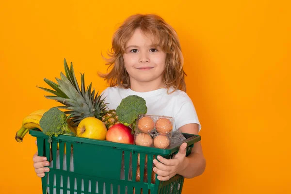 Grocery shop. Portrait of child with grocery shopping cart. Kid with shopping basket, isolated on yellow studio background