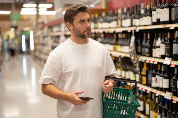 Man with grocery basket shopping at supermarket. Man choosing alcohol bottles at liquor store