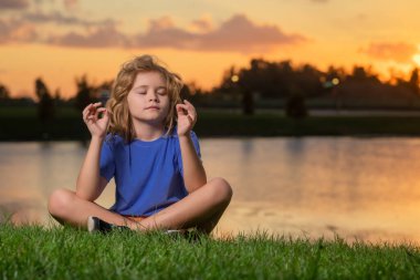 Çocuk sükuneti ve doğal arka planda rahatlama. Küçük çocuk yoga yaparken meditasyon yapıyor. Özgürlük ve tasasız konsept. Bahar günbatımında dışarıda meditasyon.