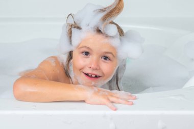 Sabun köpüklü banyo küveti. Küvette köpükle oynayan tatlı sarışın çocuk. Mutlu çocuk gülümsüyor ve kameraya bakıyor. Tasasız çocukluk. Küçük çocuk büyük miktarda köpükle banyo yapıyor.