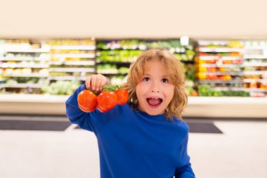 Taze domates sebzeli çocuk. Sebze süpermarketindeki çocuk. Küçük çocuk markette ya da markette yemek seçiyor.