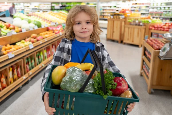 Happy little kid with fruits and vegetables at grocery store. Healthy food for young family with kids. Happy child with shopping cart full of fresh vegetables. Kids at grocery store or supermarket