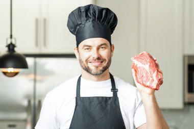 Aşçı yamağı etli biftek. Aşçı üniformalı, çiğ et filetosu olan bir erkek şef. Aşçı mutfakta çiğ et pişiriyor.