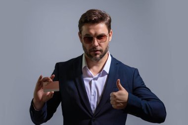 Gri arka planda kredi kartı tutan bir iş adamı. İspanyol adam kredi kartını gösteriyor. Kredi kartı ya da banka kartı. İnternetten alışveriş konsepti. İndirim teklifi, online alışveriş.