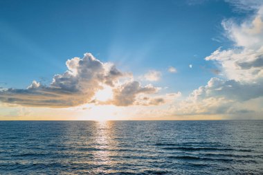 Calm sea with sunset sky and sun through the clouds over. Sunrise sea on tropical beach. Landscape of beautiful beach. Beautiful sunset at sea. Ocean sunset on sky background with colorful clouds