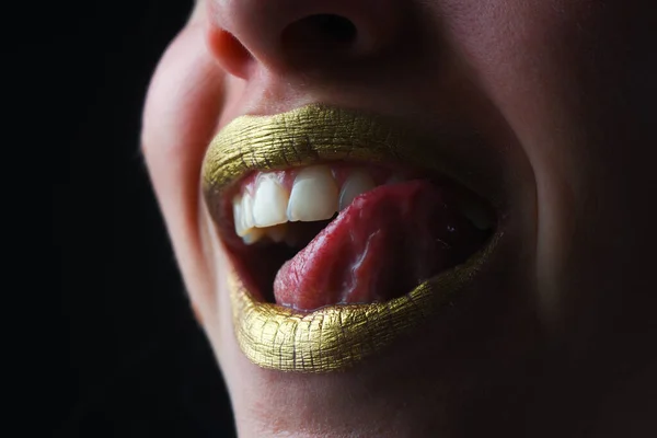 Sexy tongue licking lips. Sensual happy smiling woman mouth. Sexy girl golden lips, gold mouth. Glowing gold skin and gild lips. Metallic shine golden lip gloss