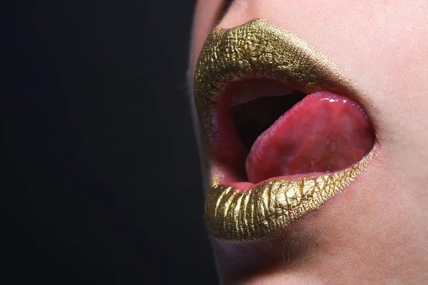 Sensual tongue licking lips. Gold paint on mouth. Golden lips. Luxury gold lips make-up. Golden lips with creative metallic lipstick. Gold metal lip. Sensual woman mouth, clse up, macro