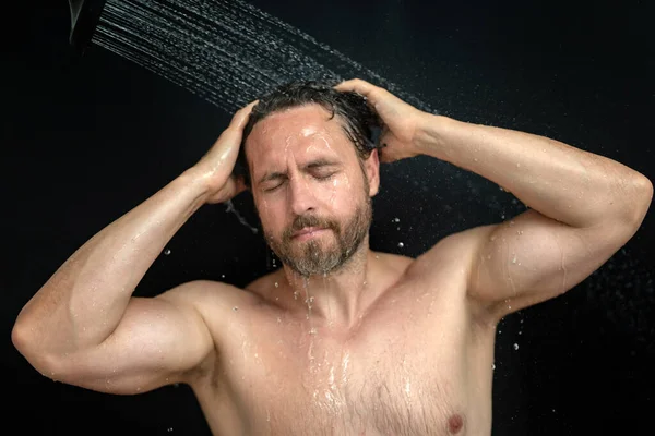 Millennial man washing hair in bath. Guy bathing shower head in bathtub. Face in foam in shower. Bathing man taking shower. Closeup guy showering. Shower concept. Man is under water drops in showers