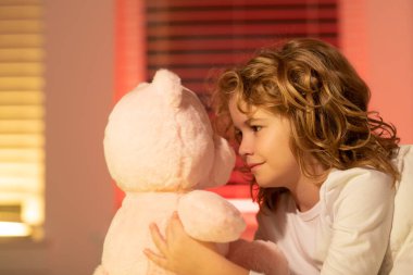 Oyuncak ayıyla oynayan bir çocuk. Yatağında oyuncak ayısı olan tatlı, uykulu bir çocuk, yatma zamanı, çocukluk dönemi ve büyüyen çocuklar konsepti, kapalı mekan portresi. Uykulu bir çocuk.