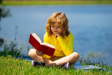 Kid read a book. Early education for kids. Summer vacation with reading book. Outdoor homework. Summer camp with book. Kids reading and education concept. Kid sitting on grass and reading a book