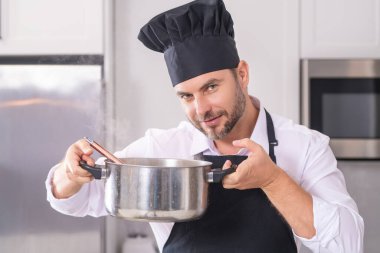 Aşçı adam mutfakta tencerede yemek pişiriyor. Gurme yemeği hazırlama süreci. Adam evde yemek pişiriyor, esrar kullanıyor. Şef yemek pişiriyor. Yakışıklı aşçı aşçı konsepti