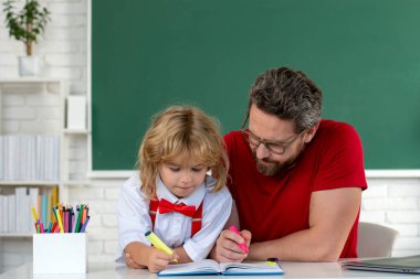 İlkokul çocuğu derste sınıfta. Öğretmen öğrenciye açıklıyor. Eğitim ve öğrenme kavramı. Baba ve oğul okulda ödev yapıyor.