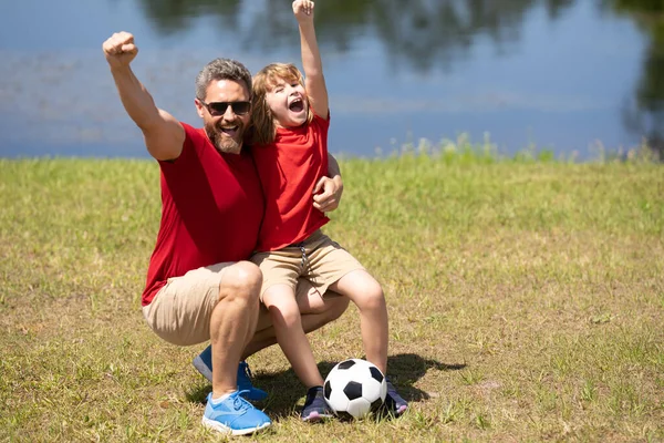 Excited father with son football team winning. Excited father with son playing football at the field. Father and son play soccer. They both feel a sense of camaraderie as they play as a team