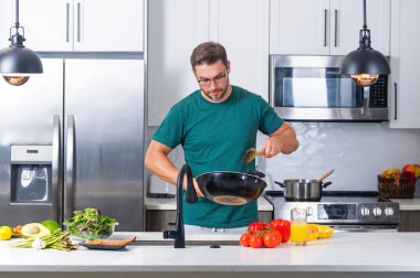 Aşçı mutfakta tavayla yemek pişiriyor. Şef aşçı tavayla hazırlar. Aşçı modern mutfakta tavayla yemek pişiriyor. Olgun aşçı adam mutfakta durup yemek hazırlıyor.