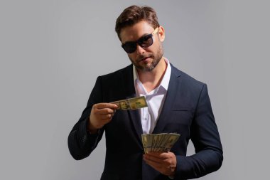 İşadamı, gri stüdyonun izole edilmiş geçmişini araştırıyor. Dolar banknotları olan takım elbiseli zengin bir adam. Dolar banknotları olan başarılı bir iş adamı. Takım elbiseli zengin milyoner