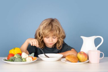 Çocuk çorba içiyor. Küçük bir çocuğun portresi çorba yerken ya da kahvaltı yaparken masada kaşıkla yemek yerken.