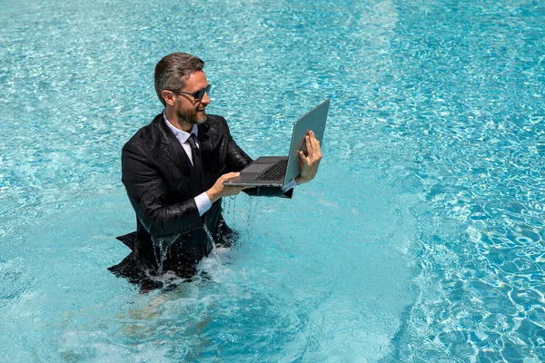 stock image Business man in suit and laptop splash water in swimming pool. Crazy summer business vacation. Funny excited amazed businessman in formal wear jump in poolside water. Hot summer business