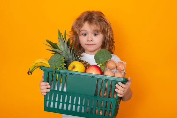 Food store. Portrait of child with shopping cart full of fresh vegetables, isolated studio background. Little child in a food store. Supermarket shopping and grocery shop concept
