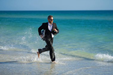 Leisure weekend and remote freelance work. Crazy comic business man in suit rest on sea bech. Funny businessman with laptop runnig on water. Remote summer business. Summer holiday for businessman