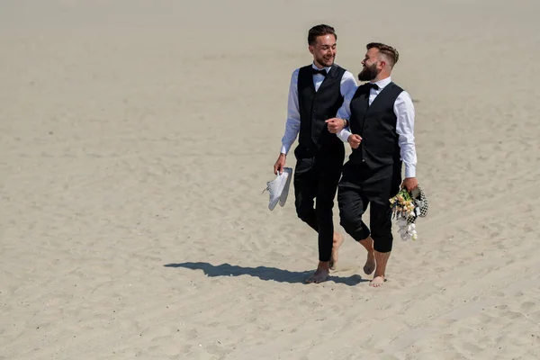 Gay couple together in love. Two gays in feeling love during wedding ceremony. Gay grooms walking together on sea beach during Wedding day. Romantic men walk on sandy beach