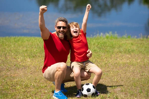 Excited father with son football team winning. Dad and little boy play soccer. Sporty family enjoy summer day. Healthy sport kids. Football soccer game. Fathers day. Successful family play football