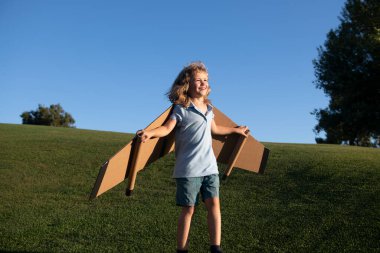 Çocuk yaz parkında oyuncak uçak kanatlarıyla oynuyor. Yenilik teknolojisi ve başarı konsepti. Çocuk pilot parkta çimlerde eğleniyor. Mutlu çocuk dışarıda oynuyor.