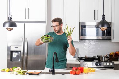 Mutfakta yemek yapan orta yaşlı bir adam. Mutfakta sebzeli adam. Mutfakta sebze malzemeleriyle yemek pişiren sıradan bir adamın portresi. Adam mutfakta salata hazırlıyor.