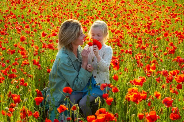 Happy spring family. Beautiful mother and daughter in spring poppy flower field. Happy family resting on a beautiful poppy field. Mom holds her child daughter in the flowering meadow