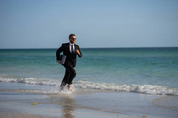 Excited summer business travel. Freelance work, online working. Summer businessman in suit run in sea water. Freelance travel. Funny freelancer in suit jump and run in the sea. Freelance and holidays