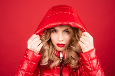Kırmızı ceketli ve kapüşonlu manken. Stüdyoda şık bir kadın moda elbisesi giyiyor. Güzel kız moda kıyafetleri giyer. Günlük kıyafet, moda tarzı.