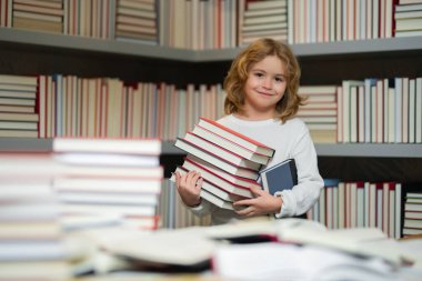 Okul çocuğu bir yığın kitap tutuyor. Entelektüel çocuk, zeki öğrenci. Bir sürü kitabı olan okul çocuğu. Çocuklar okul kütüphanesinde kitap hikayesinin keyfini çıkarıyorlar. Çocukların hayal gücü, edebiyat ilgisi