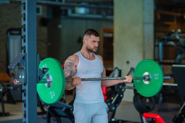 Kas yığını adam spor salonunda dambıllarla antrenman yapıyor. Spor salonunda poz veren kaslı yakışıklı bir adam. Kas sporcusu dambılı kaldırıyor. Spor kulübünde esneme, spor egzersizleri.