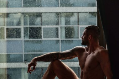 Sexy and naked muscular young man posing on window curtains. Sexy shirtless male model. Attractive young naked man body. Romantic dreaming nude male model with sexy body