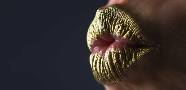 Kiss. Close up woma face with gold lips. Gold paint on mouth. Golden lips. Luxury gold lips make-up. Golden lips with creative metallic lipstick. Gold metal lip. Sensual woman mouth, clse up, macro
