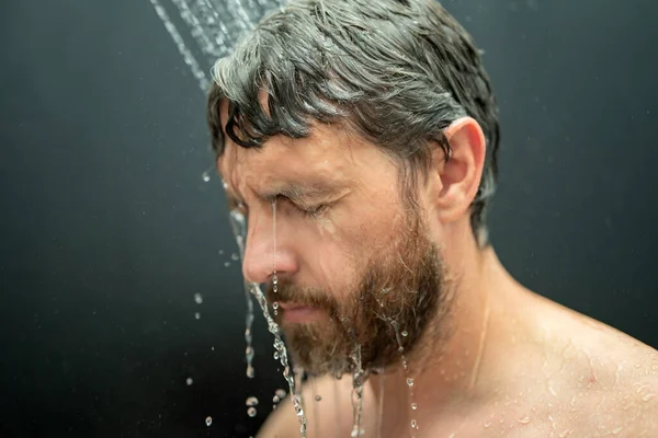 Millennial man washing hair in bath. Guy bathing shower head in bathtub. Face in foam in shower. Bathing man taking shower. Closeup guy showering. Shower concept. Man is under water drops in showers