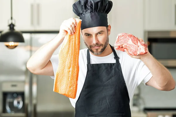 Chef with raw meat beef and fish salmon fillet on kitchen. Chef man in uniform on kitchen. Handsome man chef in uniform with chef hat cooking raw meat beef and fish salmon fillet in the kitchen