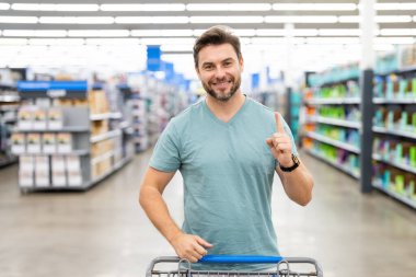 Dükkanda alışveriş arabalı bir adamın portresi. Süpermarket alışverişi ve market konsepti. Alışverişe. Süpermarketten alışveriş sepeti alan adam.