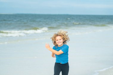 Yaz plajında heyecanlı bir çocuk koşusu. Kumsalda koşan tatlı çocuk yaz denizinin tadını çıkarıyor ve hayal kuruyor. Komik küçük çocuk yaz plajında koşuyor. Mutlu çocuk koşar ve yaz kumsalında hayatın tadını çıkarır. Çocuk koşucu
