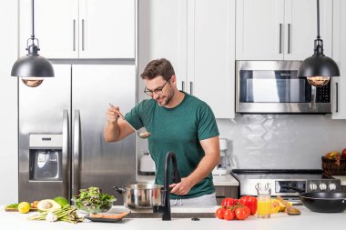 Evde yemek pişirmek. Mutfakta yemek hazırlayan adam. Erkek aşçı evde yemek hazırlıyor. Şef yemek yapıyor. Yemek pişiren adam, mutfak tenceresi, yemek tabağı. Adam mutfak içinde çorba hazırlıyor.